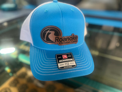 Blue and white cap with 'Roanoke Christian Camp' logo on a reflective surface